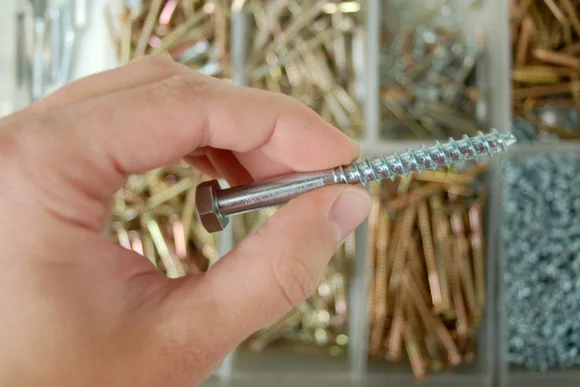 Hand hält Schraube über Schraubenbox